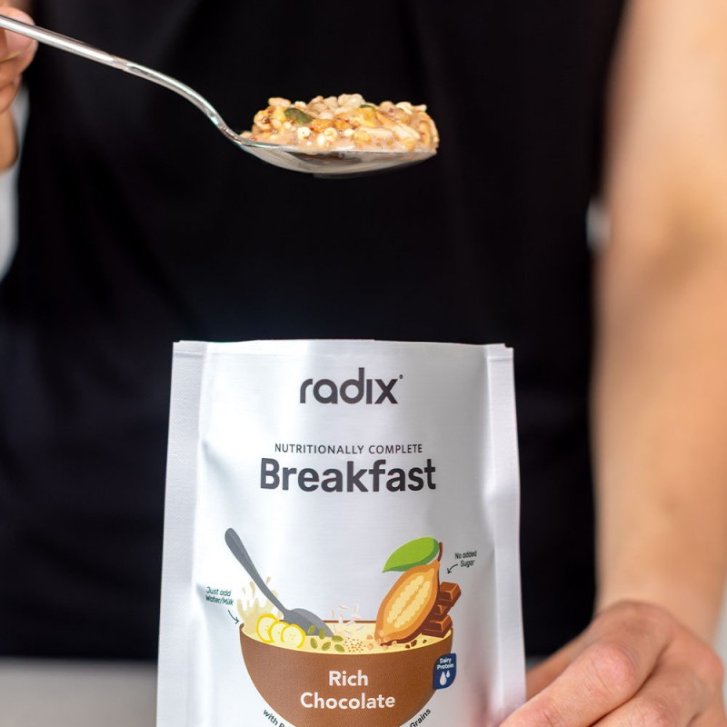 Front of Radix Rich Chocolate Breakfast pouch with brown bowl, cacao pod and chocolate bar graphic, and “NEW” label in dark brown circle