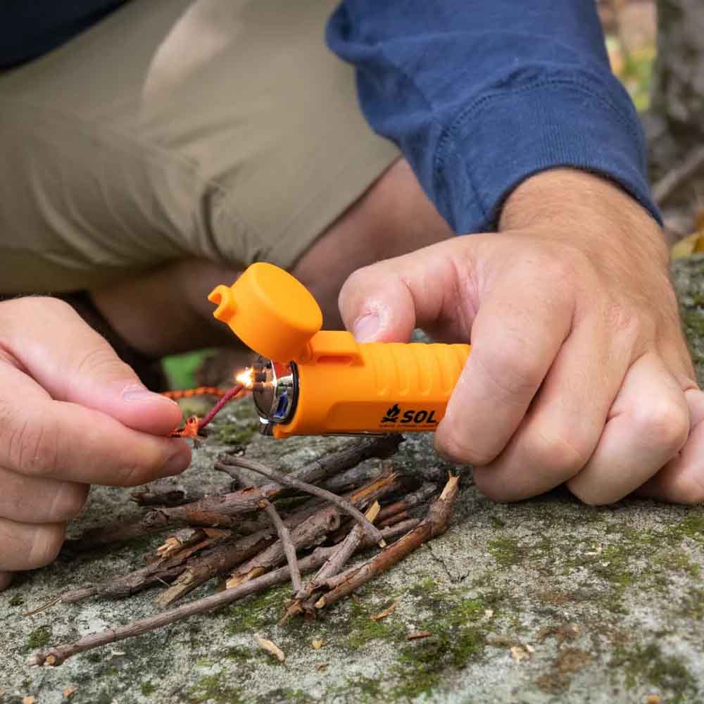 Person using the SOL Fire Lite Fuel-Free Lighter to ignite tinder in the wild during camping
