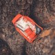 SOL Scout Survival Kit – Packed and Ready Outdoors Compact SOL Scout Survival Kit resting on tree bark, showing waterproof dry bag and fire-starting gear