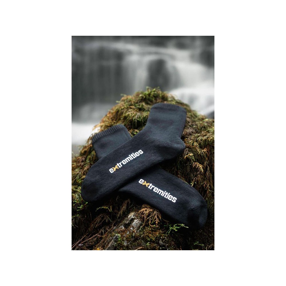 Pair of black waterproof outdoor socks displayed on mossy rocks near waterfall for hiking trekking and camping adventures