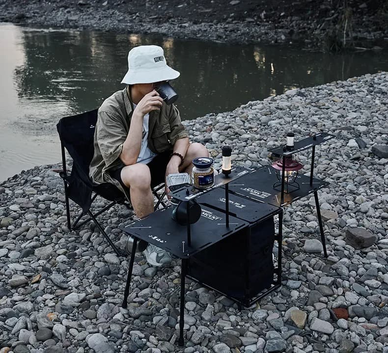 Foldable camping table fully extended with modular side tables and central black storage compartment.