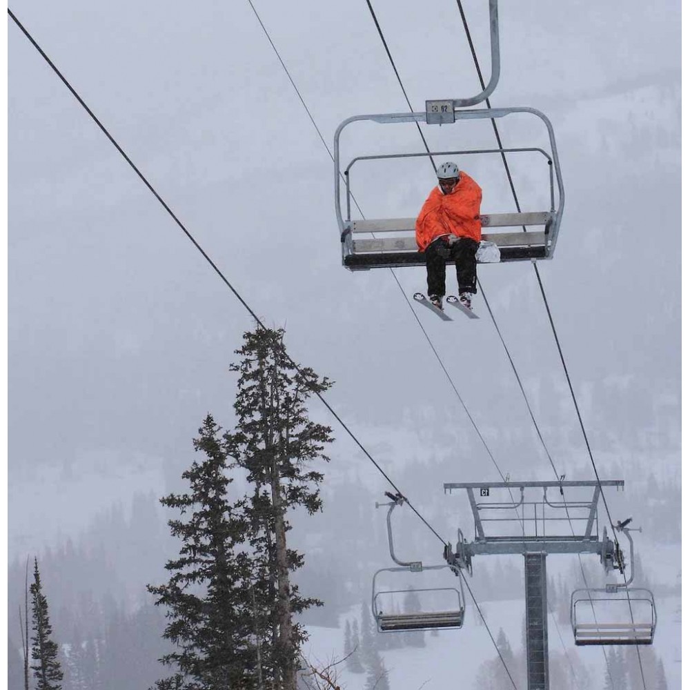 Person Using SOL Blanket XL on Ski Lift in Cold Weather Skier wrapped in SOL Emergency Blanket XL for warmth and visibility on mountain chairlift