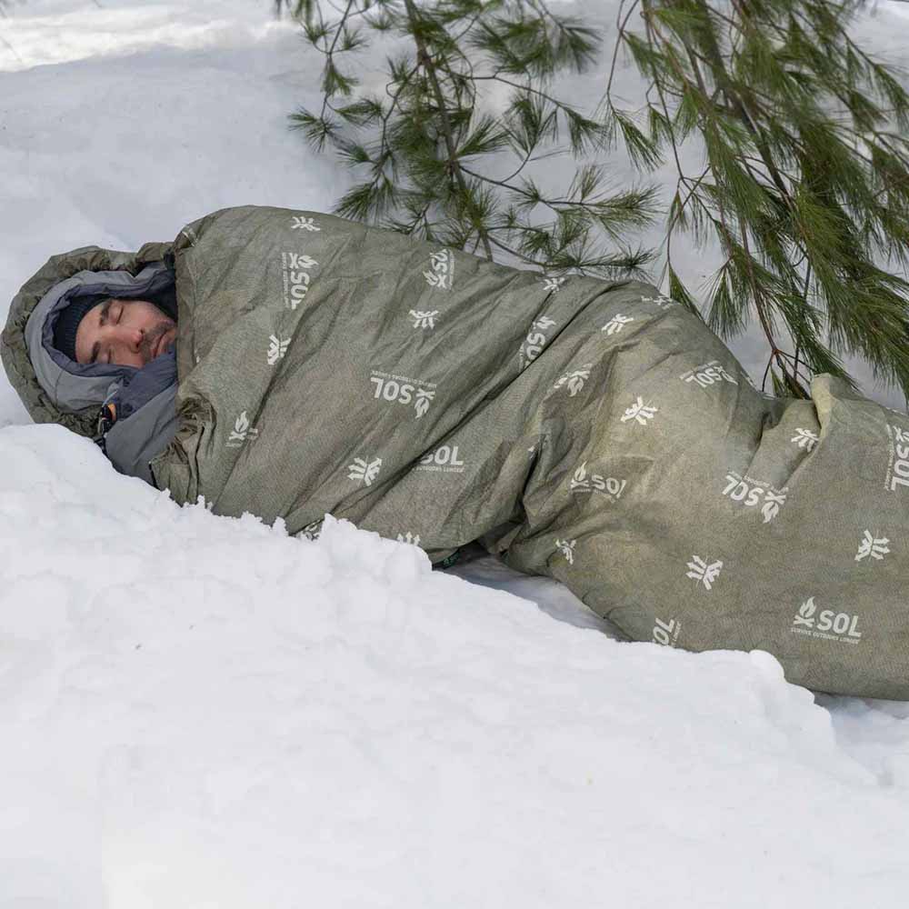 Person Sleeping in OD Green SOL Escape Bivvy in Snow Man sleeping in breathable OD Green SOL Escape Bivvy during cold weather conditions