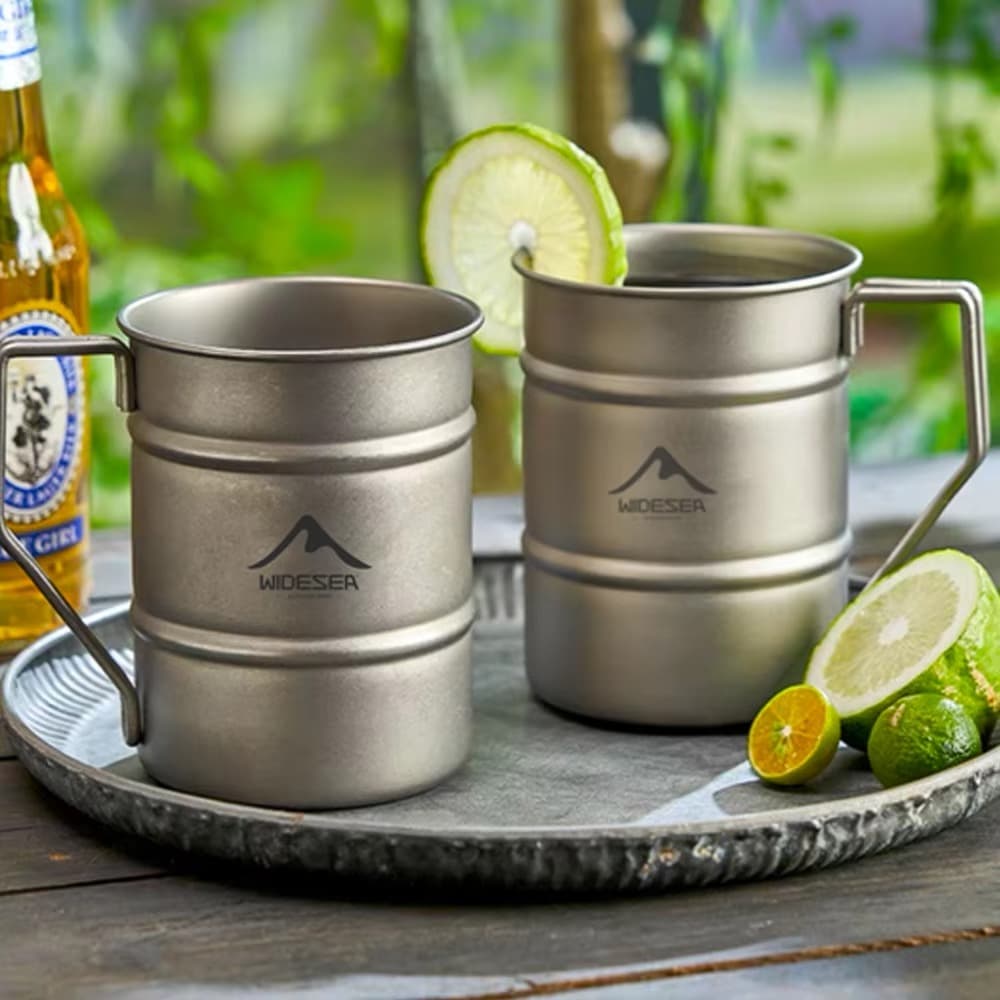 Widesea Titanium Mug for Outdoor Dining and Camping Two Widesea titanium mugs on outdoor tray with lime and beer in natural setting