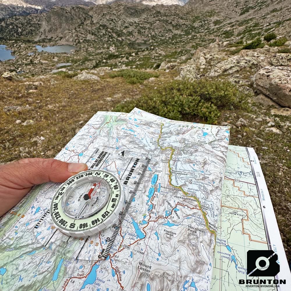 Brunton Scout Glow Compass on Map Outdoors Brunton Scout Glow Compass placed on a topographic map in a mountainous outdoor setting