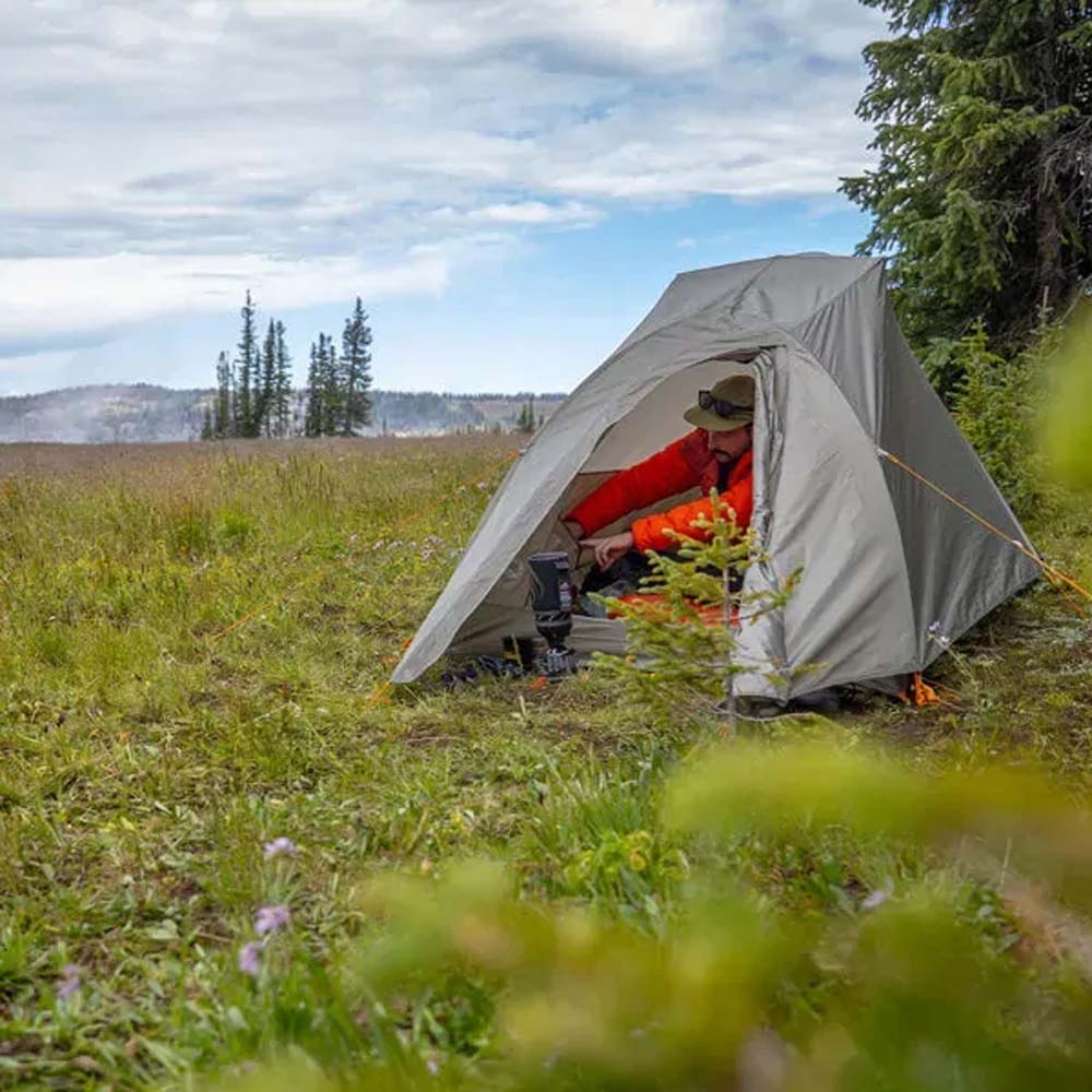 Camper sitting inside Big Agnes C Bar Tent in a grassy campsite with gear in vestibule.