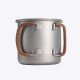 A silver titanium mug with a foldable handle and leather rope attachment, sitting on a rock beside a campfire.