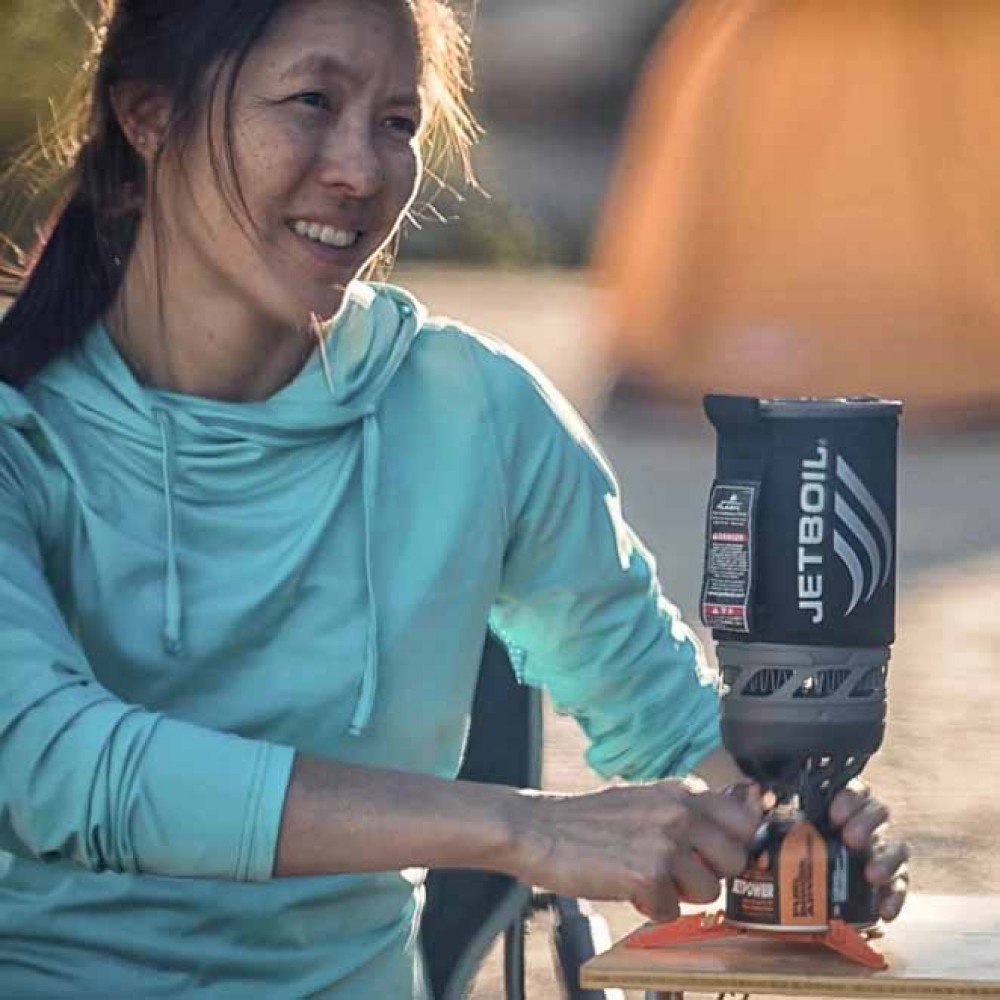 Woman Using Jetboil Flash Stove at Campsite – Outdoor Cooking Scene Camper using Jetboil Flash 1.0L stove with Jetpower fuel at campsite, smiling next to tent