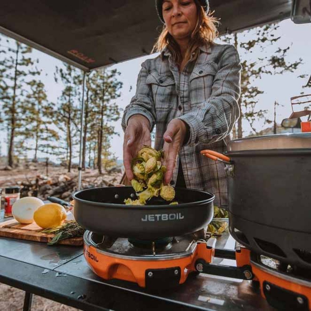Jetboil Genesis Base Camp System – Compact Outdoor Cooking Solution Woman cooking Brussels sprouts in a Jetboil frypan using the Genesis Base Camp System during a camping trip.