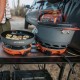 Jetboil Genesis System with Frypan and Cooking Pot in Use Jetboil Genesis Base Camp System setup on a camping table, with a frying pan and cooking pot in use next to a parked vehicle.