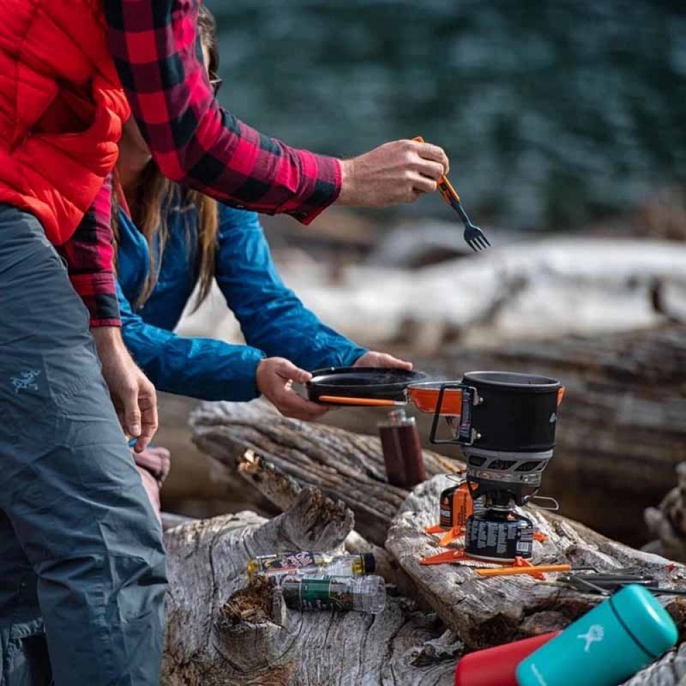 Campers Cooking with Jetboil MiniMo – Wilderness Meal Prep Campers preparing food using Jetboil MiniMo stove on a log, lakeside wilderness setting