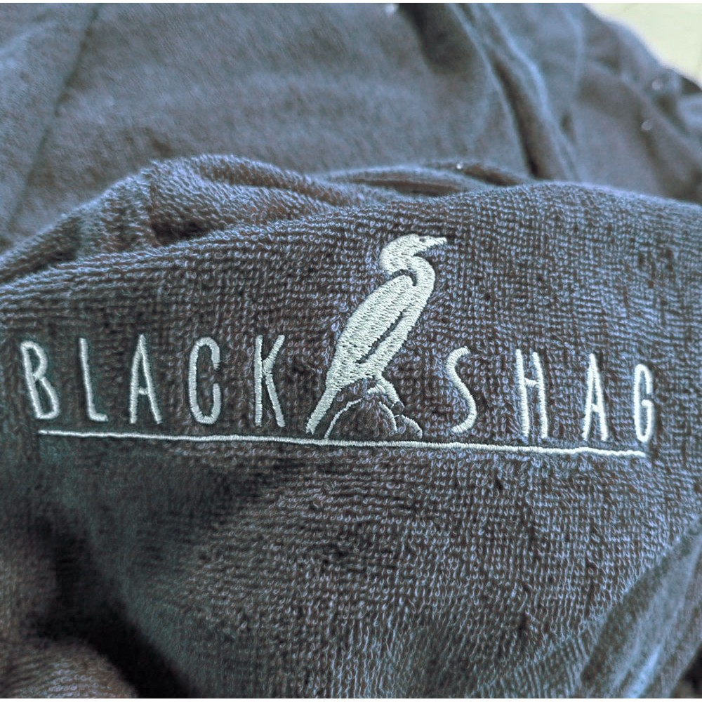 Close-up of slate blue cotton poncho towel showing soft terry fabric texture and embroidered Black Shag logo detail