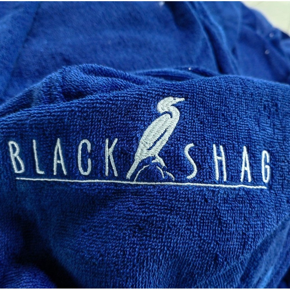 Close-up of electric blue cotton poncho towel showing soft terry fabric texture and embroidered Black Shag logo detail